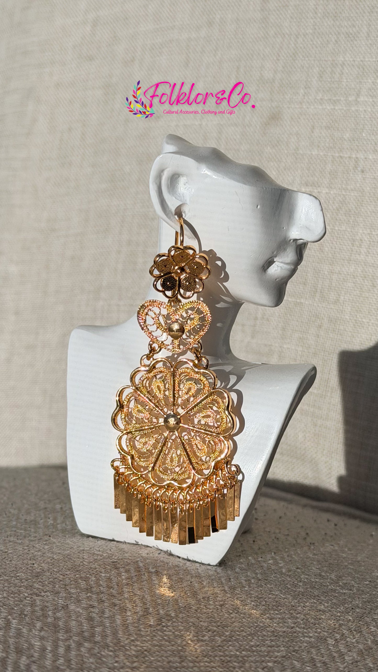 Gold earrings on a mannequin ear with 'Folkloryco' branding