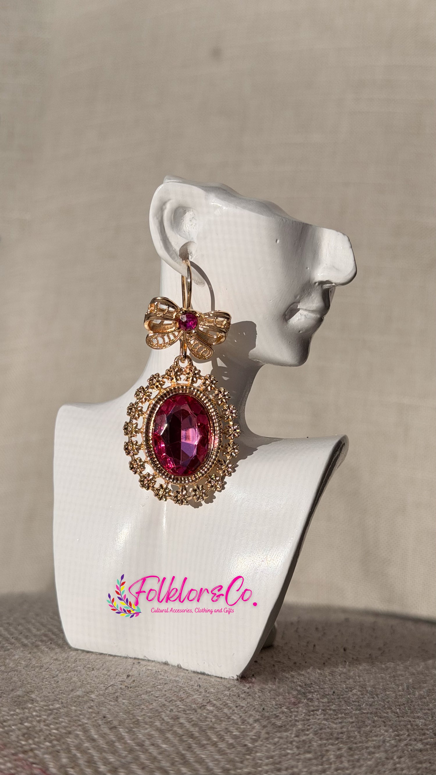 Gold and pink earrings on a white mannequin bust with 'Folkloryco' branding.