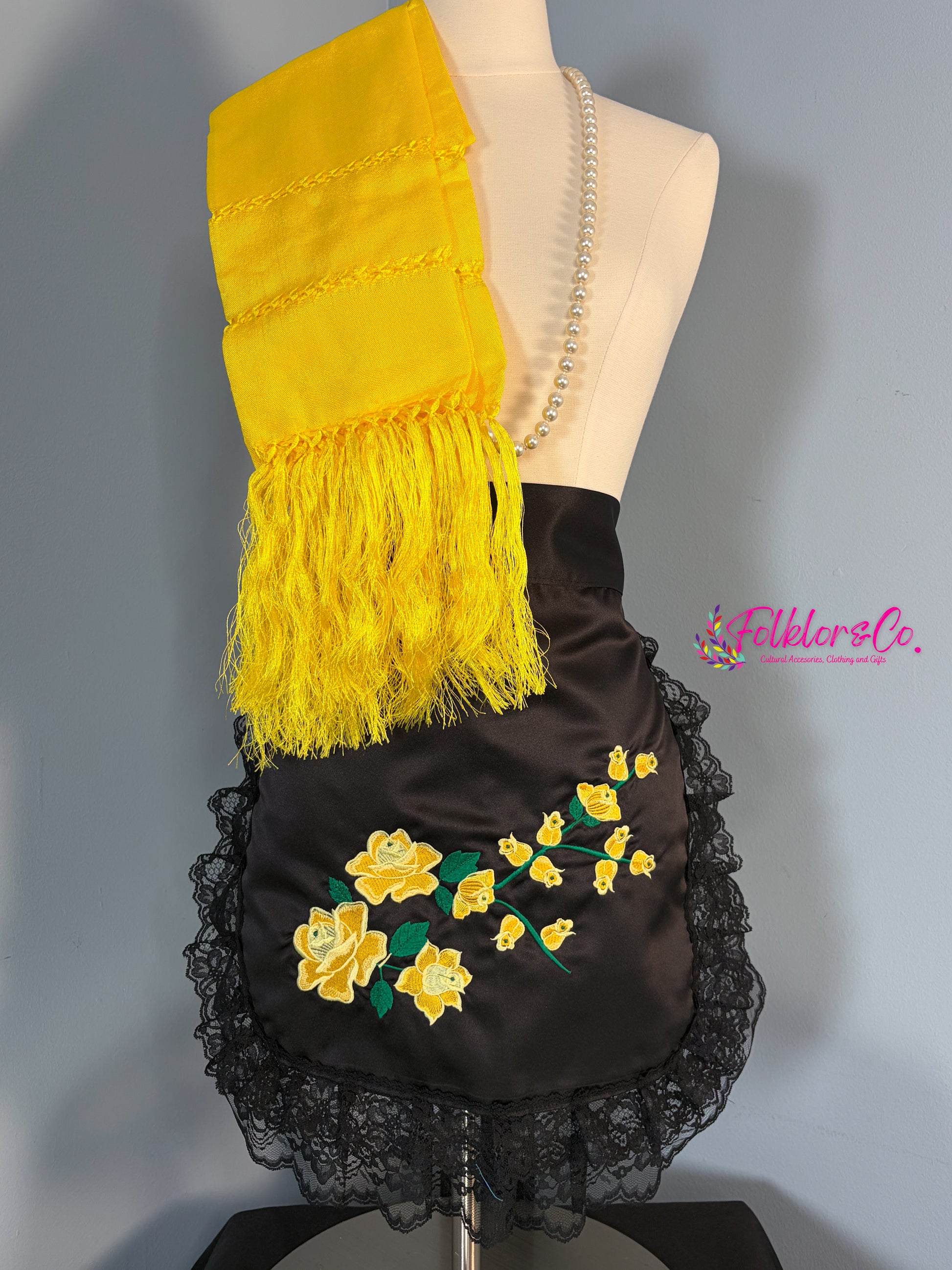 Mannequin wearing a black mandil with yellow floral embroidery and a yellow shawl with fringe.