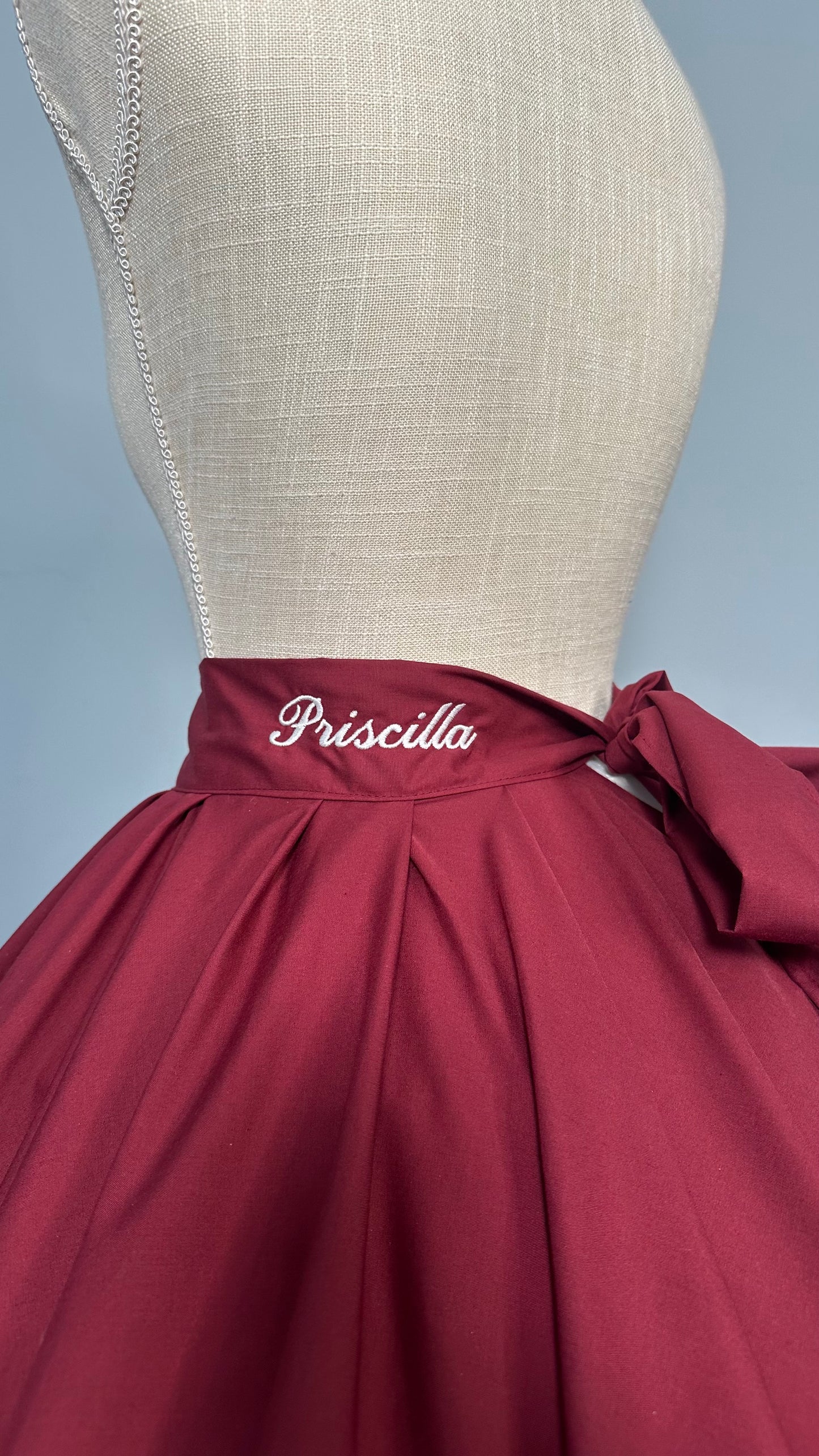 Maroon dress on a mannequin with 'Priscilla' branding against a gray background