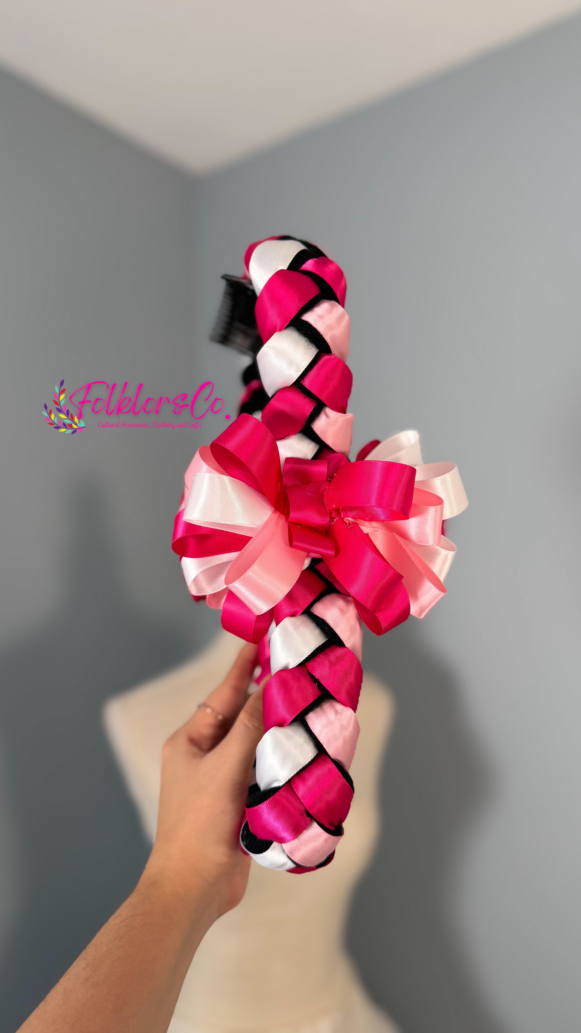 Hand holding a colorful braided Jalisco trenza against a gray background