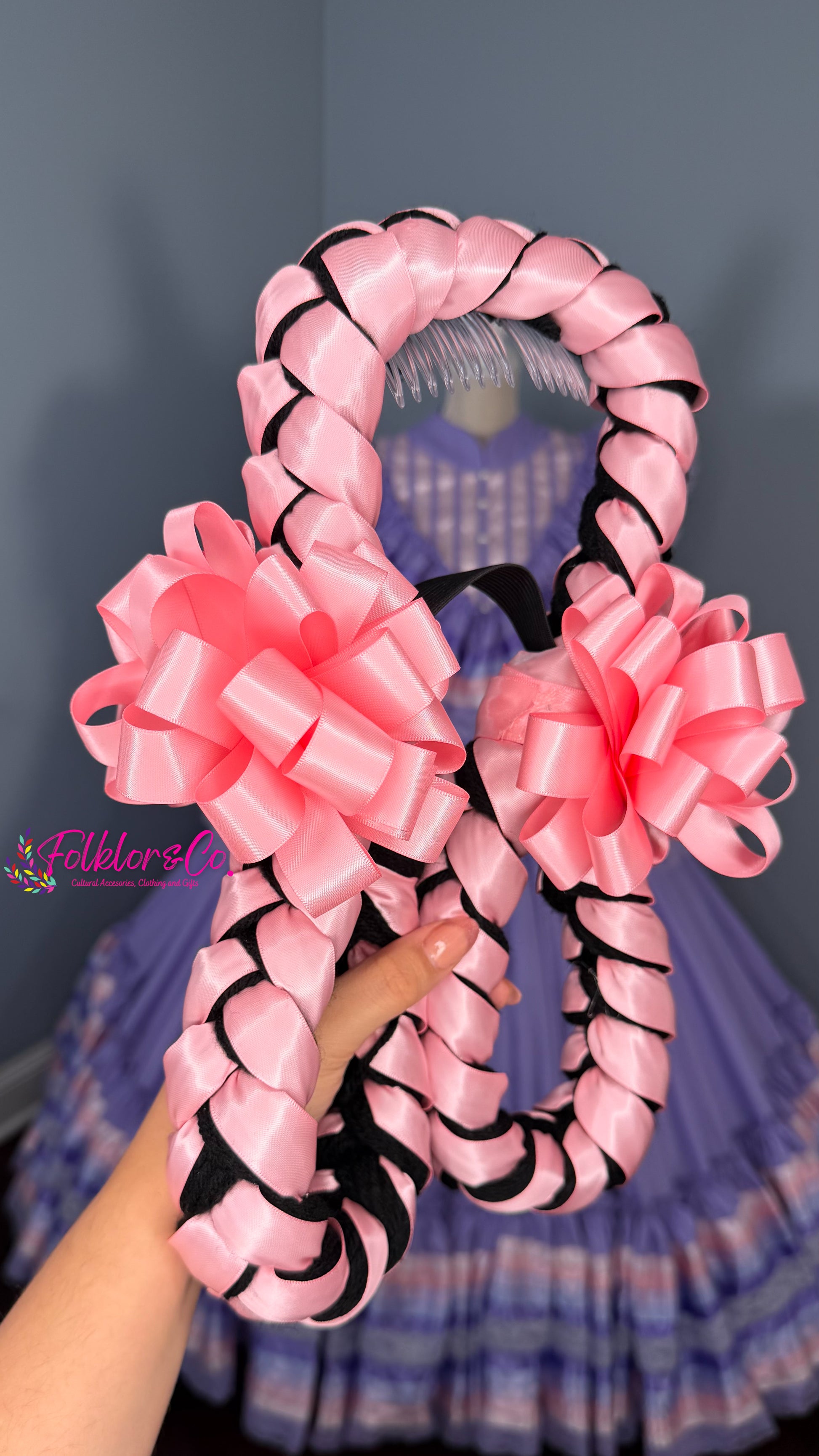 Large pink and black decorative folklorico trenza bow held by a person against a dark background