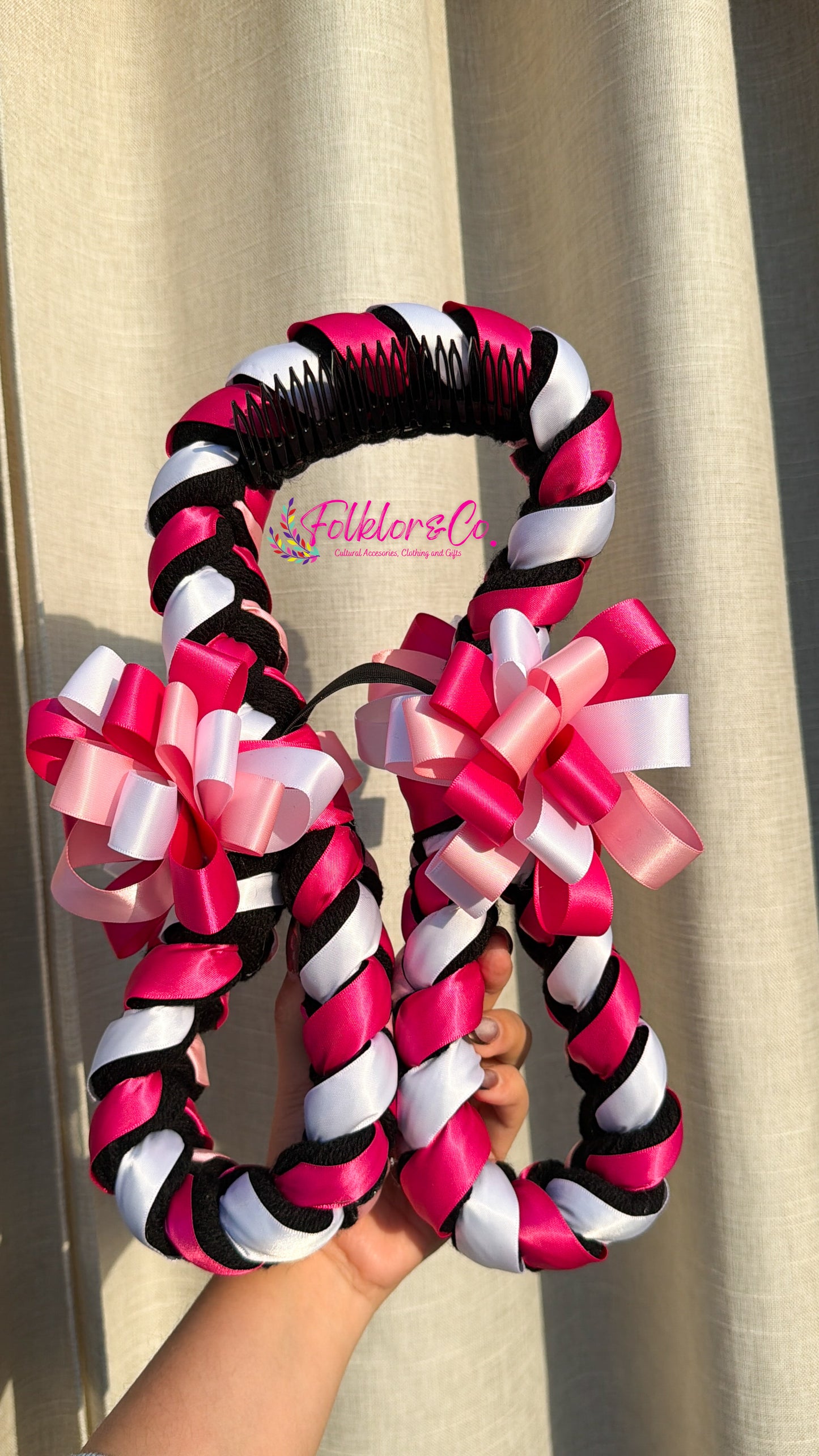 Decorative folklorico trenza with pink, white, and black ribbons held against a neutral background